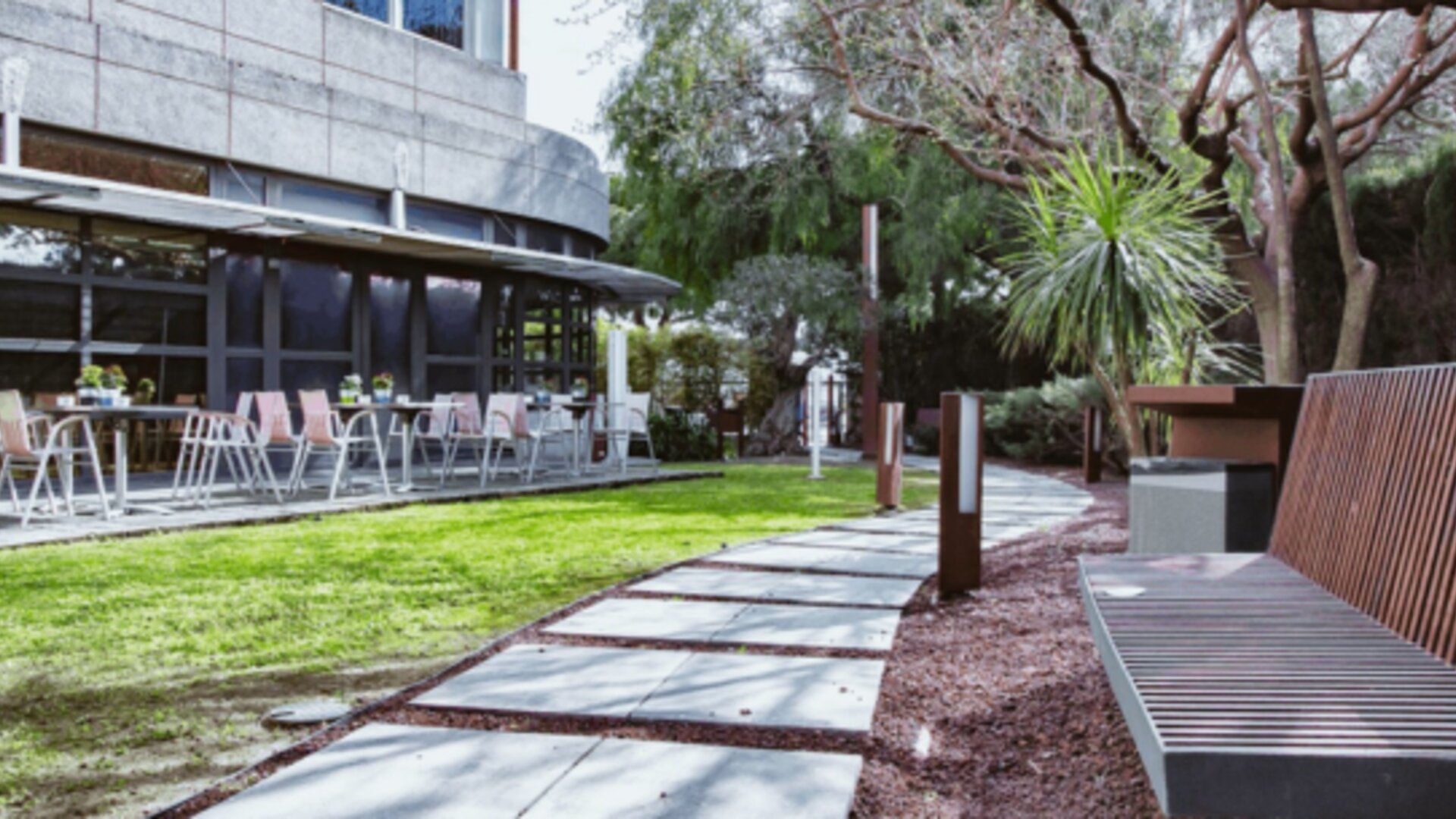 Outdoor garden walkway with a wooden bench, trees, green lawn and restaurant terrace at Hotel Best Western PLUS Alfa Aeropuerto.