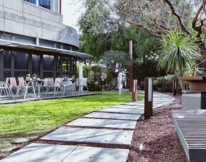 Outdoor garden walkway with a wooden bench, trees, green lawn and restaurant terrace at Hotel Best Western PLUS Alfa Aeropuerto.