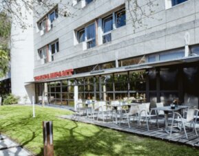 Outdoor restaurant terrace with white tables and chairs beside a landscaped lawn and modern hotel building at Hotel Best Western PLUS Alfa Aeropuerto.