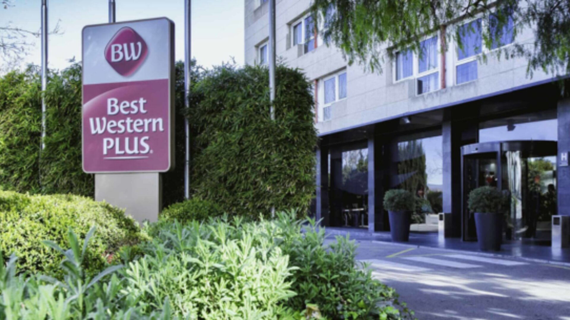 Modern hotel exterior with Best Western PLUS signage, glass entrance and landscaped greenery at Hotel Best Western PLUS Alfa Aeropuerto.