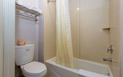 Private guest bathroom at Buena Vista Inn featuring a bathtub with shower, cream-colored shower curtain, toilet, and wall-mounted shelving stocked with fresh towels.