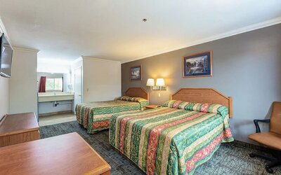 Spacious guest room at Buena Vista Inn featuring two beds with colorful patterned bedspreads, wooden furniture, wall-mounted lighting, a television, and a vanity area.