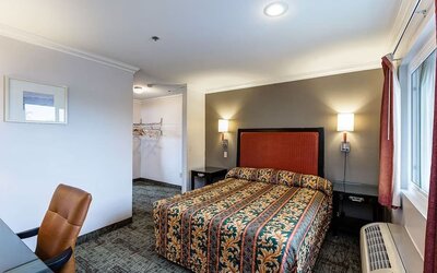 Guest room at Buena Vista Inn featuring a king-size bed with an ornate patterned bedspread, red upholstered headboard, bedside lighting, writing desk, and window with burgundy curtains.