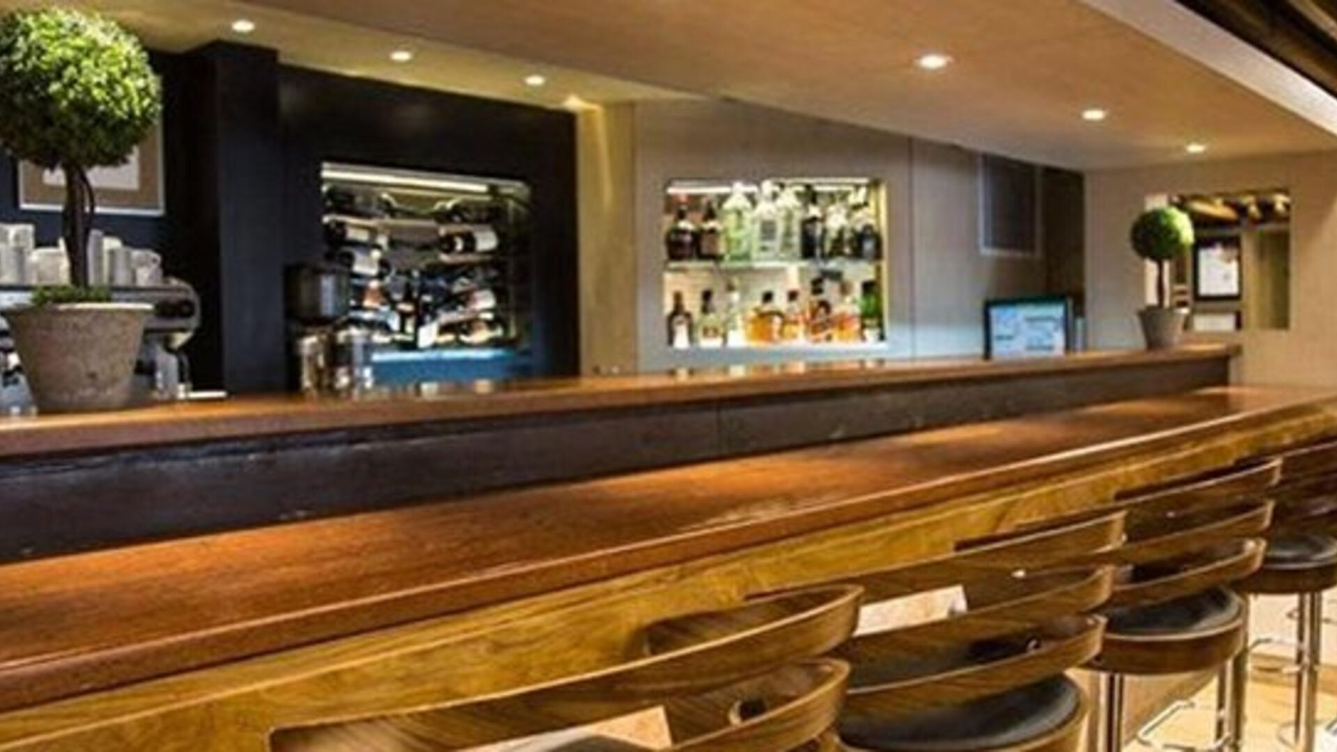 Long wooden bar counter lined with stools, backed by shelves of wine bottles and drinks at Hotel Regente Palace.