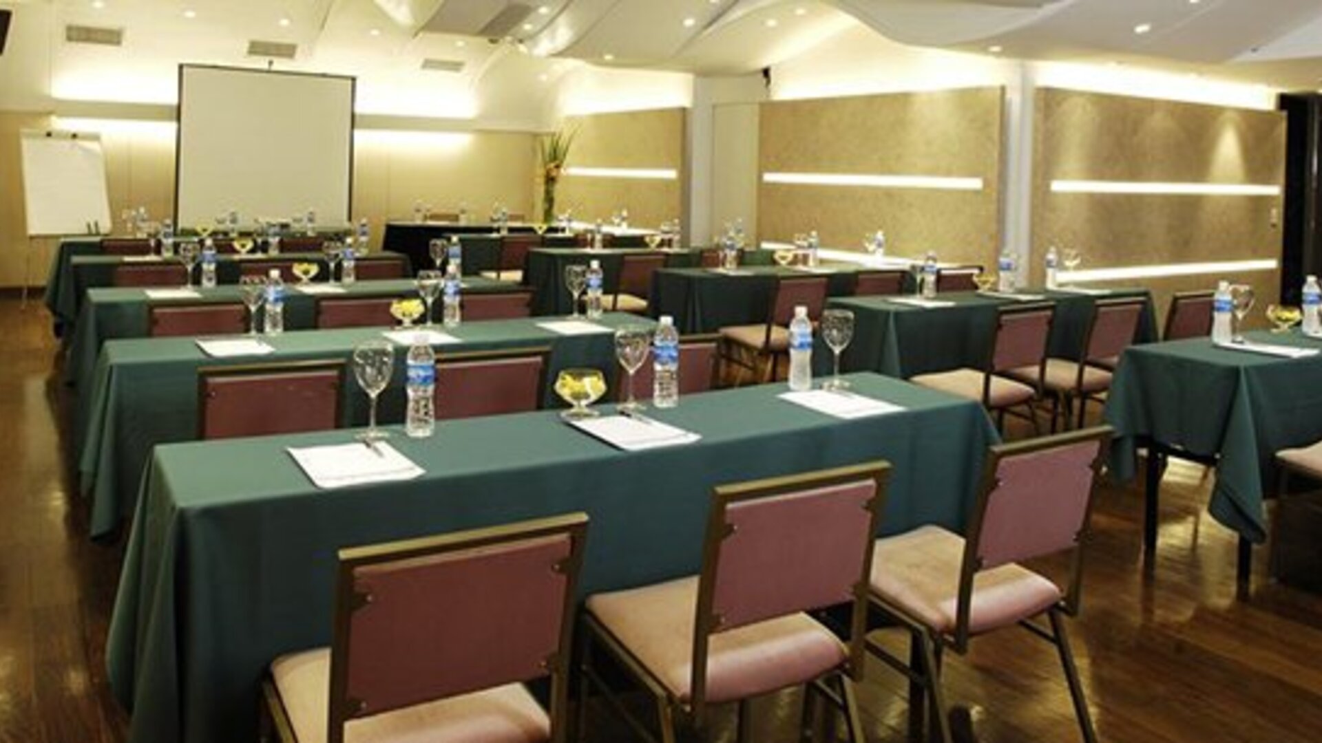 Meeting room arranged with green tablecloths, rows of chairs, water bottles and a projection screen at Hotel Regente Palace.