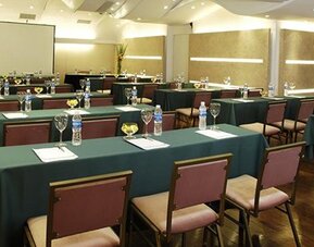 Meeting room arranged with green tablecloths, rows of chairs, water bottles and a projection screen at Hotel Regente Palace.