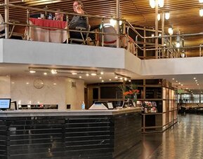 Hotel reception with black front desk, upper-level dining area, metal railings and wooden slat ceiling at Hotel Regente Palace.
