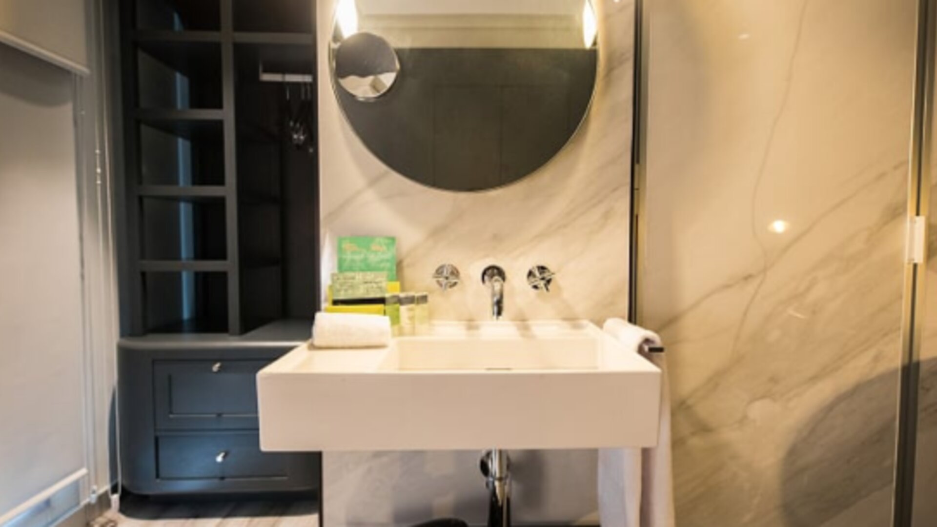 Modern bathroom with white vessel sink, round mirror, marble-effect walls and dark built-in shelving at Hotel Silken Saaj Las Palmas.Meeting room with neatly arranged tables, dark chairs, white place settings and warm recessed lighting at Hotel Silken Saa