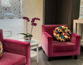 Lobby lounge with magenta armchairs, colourful cushions, purple orchids and patterned decorative panels at Ian Hotel.
