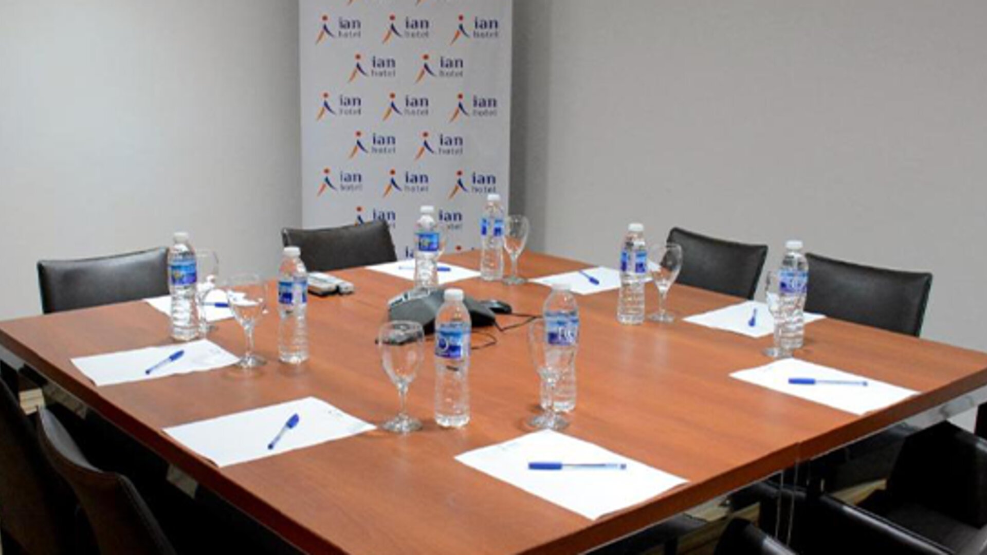 Meeting room with wooden conference table, black chairs, bottled water, glasses and notepads at Ian Hotel.