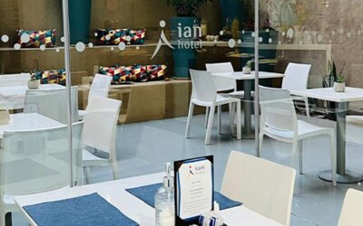 Dining area with white tables, chairs, blue placemats and glass doors overlooking a courtyard at Ian Hotel.