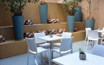 Outdoor dining patio with white tables and chairs, tall blue planters and colourful cushions at Ian Hotel.
