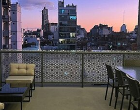 Rooftop terrace with lounge seating, dining table and city skyline views at sunset at Ian Hotel.