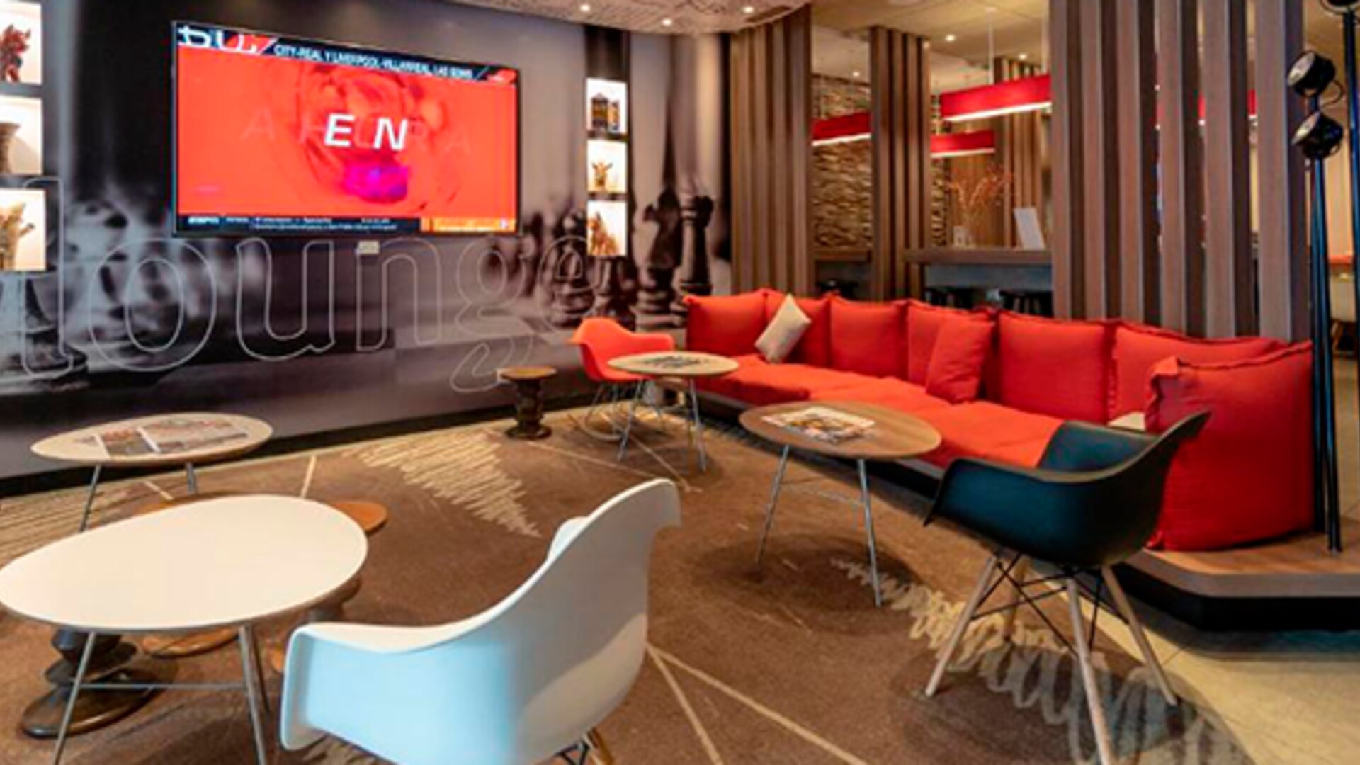 Lounge area with red sectional sofa, white and colored chairs, low tables and decorative wall graphics at Ibis Lima Reducto Miraflores.
