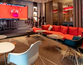 Lounge area with red sectional sofa, white and colored chairs, low tables and decorative wall graphics at Ibis Lima Reducto Miraflores.