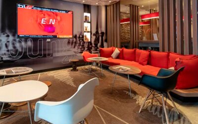 Lounge area with red sectional sofa, white and colored chairs, low tables and decorative wall graphics at Ibis Lima Reducto Miraflores.