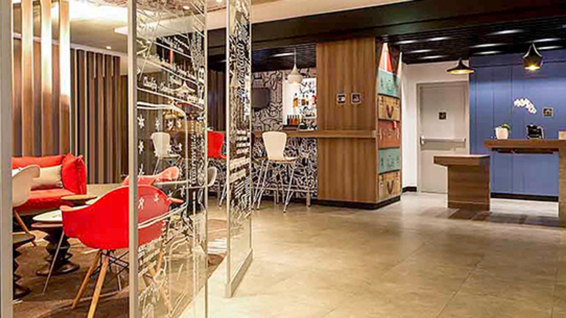 Reception and lounge area with wooden counters, blue wall panels, pendant lighting and red seating at Ibis Lima Reducto Miraflores.