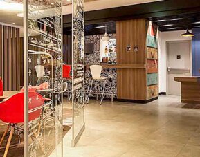 Reception and lounge area with wooden counters, blue wall panels, pendant lighting and red seating at Ibis Lima Reducto Miraflores.