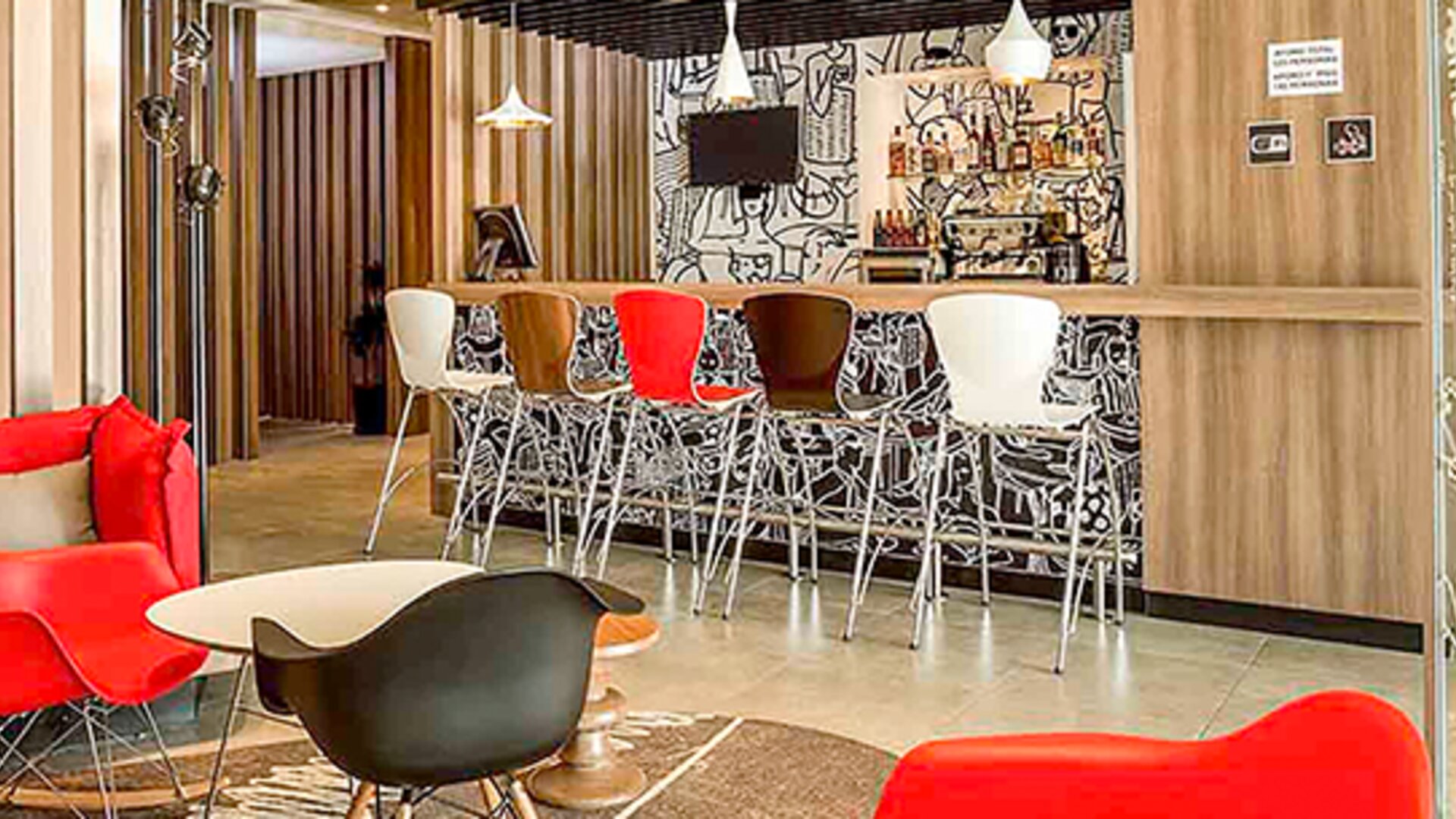 Hotel lounge with red sofas, colorful chairs, round coffee tables and patterned carpet at Ibis Lima Reducto Miraflores.