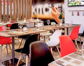 Restaurant with wooden tables, red and white chairs, place settings and decorative wall panels at Ibis Lima Reducto Miraflores.