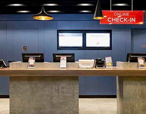 Hotel reception with long wooden counter, blue wall panels, computer stations and hanging pendant lights at Ibis Lima Reducto Miraflores.