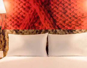 Close view of a double bed with white pillows, red decorative headboard and matching wall lamps at Ibis Lima Reducto Miraflores.