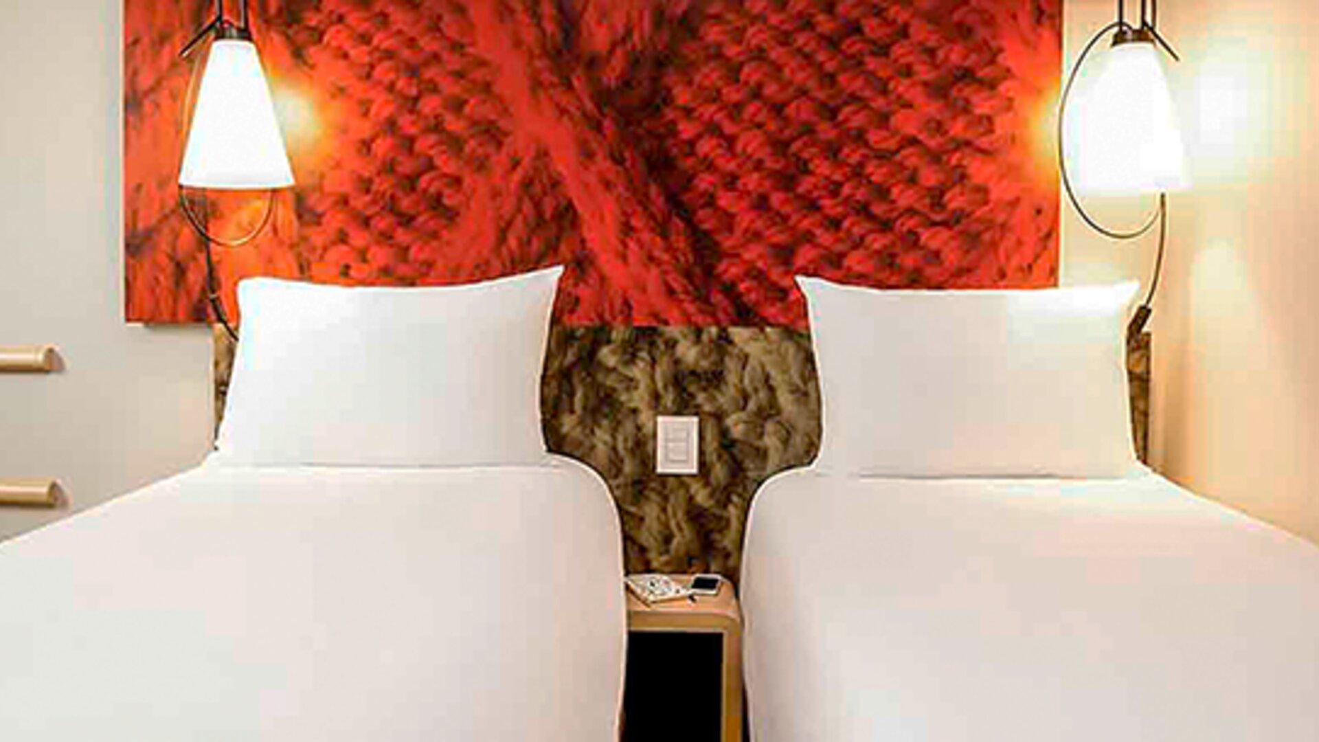 Twin beds with white linens, red textured headboard panels, bedside tables and wall-mounted lamps at Ibis Lima Reducto Miraflores.