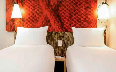 Twin beds with white linens, red textured headboard panels, bedside tables and wall-mounted lamps at Ibis Lima Reducto Miraflores.