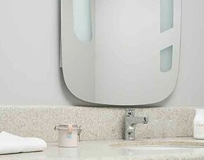 Bathroom vanity with speckled countertop, white sink, wall mirror, toiletries and folded towel at Ibis Lima Reducto Miraflores.