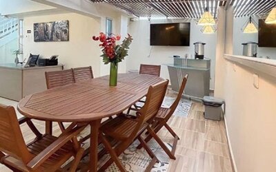 Dining area with wooden table and chairs, flower arrangement, pendant lights and staircase at 12 Nights Hotel.