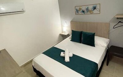 Guest room with double bed, teal bedding accents, wall-mounted television, air conditioner and open clothes rail at 12 Nights Hotel.