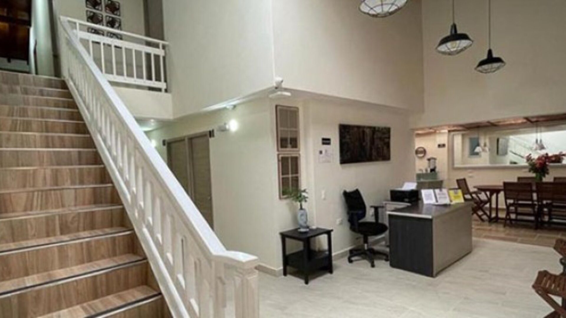 Hotel lobby with staircase, white railings, reception desk, office chair and dining area at 12 Nights Hotel.