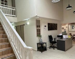 Hotel lobby with staircase, white railings, reception desk, office chair and dining area at 12 Nights Hotel.