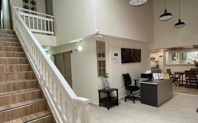Hotel lobby with staircase, white railings, reception desk, office chair and dining area at 12 Nights Hotel.