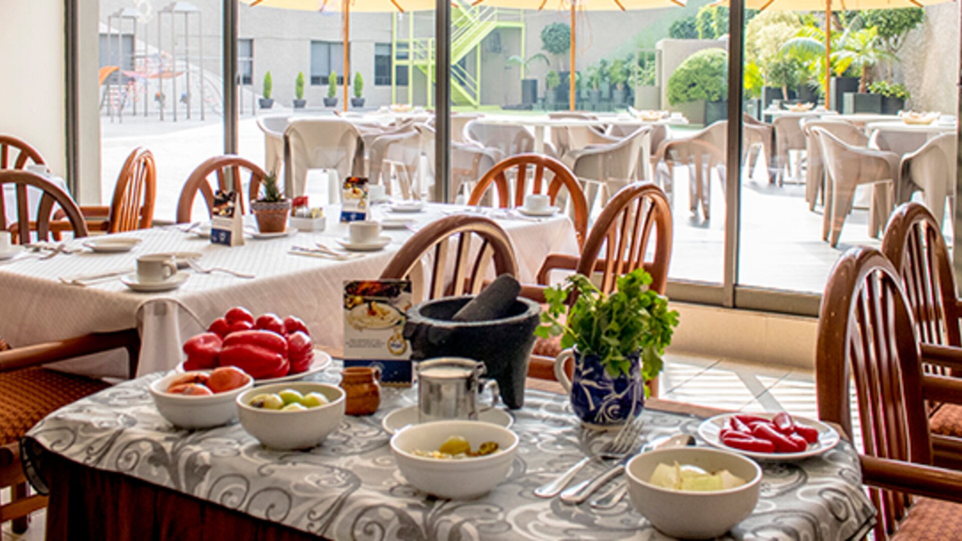Restaurant dining area with wooden chairs, white tablecloths, place settings and a central buffet counter at Hotel Misión Toreo Centro De Convenciones.