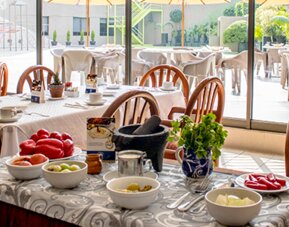 Restaurant dining area with wooden chairs, white tablecloths, place settings and a central buffet counter at Hotel Misión Toreo Centro De Convenciones.