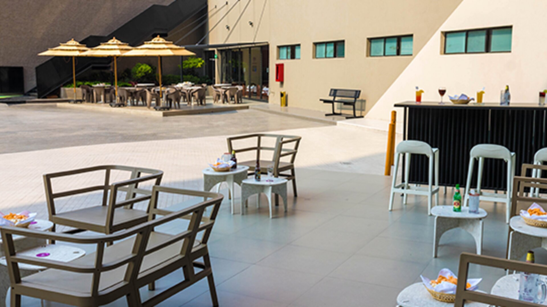 Outdoor seating area with tables, chairs, bar counter and umbrellas on a paved terrace at Hotel Misión Toreo Centro De Convenciones.