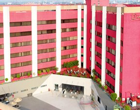 Multi-storey hotel exterior with pink and white façade, green accents and landscaped entrance at Hotel Misión Toreo Centro De Convenciones.