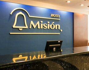 Hotel reception with black marble counter, blue feature wall and gold Hotel Misión signage at Hotel Misión Toreo Centro De Convenciones.