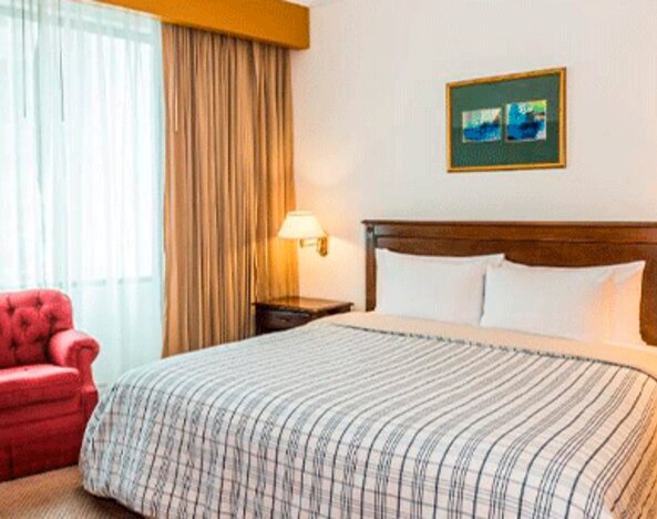Guest room with double bed, striped bedding, red armchair, bedside lamps and a large curtained window at Hospedium Princess Hotel Panamá.