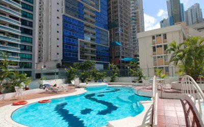 Outdoor swimming pool with turquoise water, sun loungers, palm trees and surrounding high-rise buildings at Hospedium Princess Hotel Panamá.
