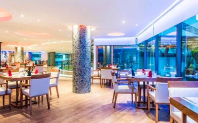 Hotel restaurant with neatly arranged tables, upholstered chairs, pendant lights and floor-to-ceiling windows at Hospedium Princess Hotel Panamá.
