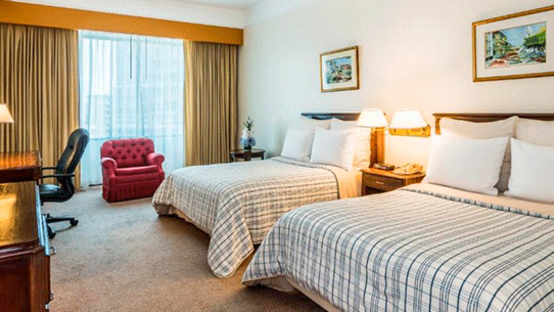 Twin guest room with two beds, striped bedding, red armchair, desk, television and large curtained window at Hospedium Princess Hotel Panamá.