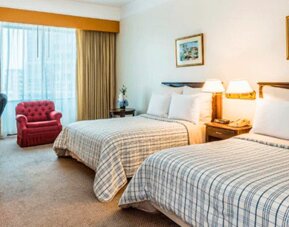 Twin guest room with two beds, striped bedding, red armchair, desk, television and large curtained window at Hospedium Princess Hotel Panamá.