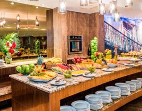 Breakfast buffet with fresh fruit, pastries, stacked plates and serving counters under pendant lighting at Hospedium Princess Hotel Panamá.