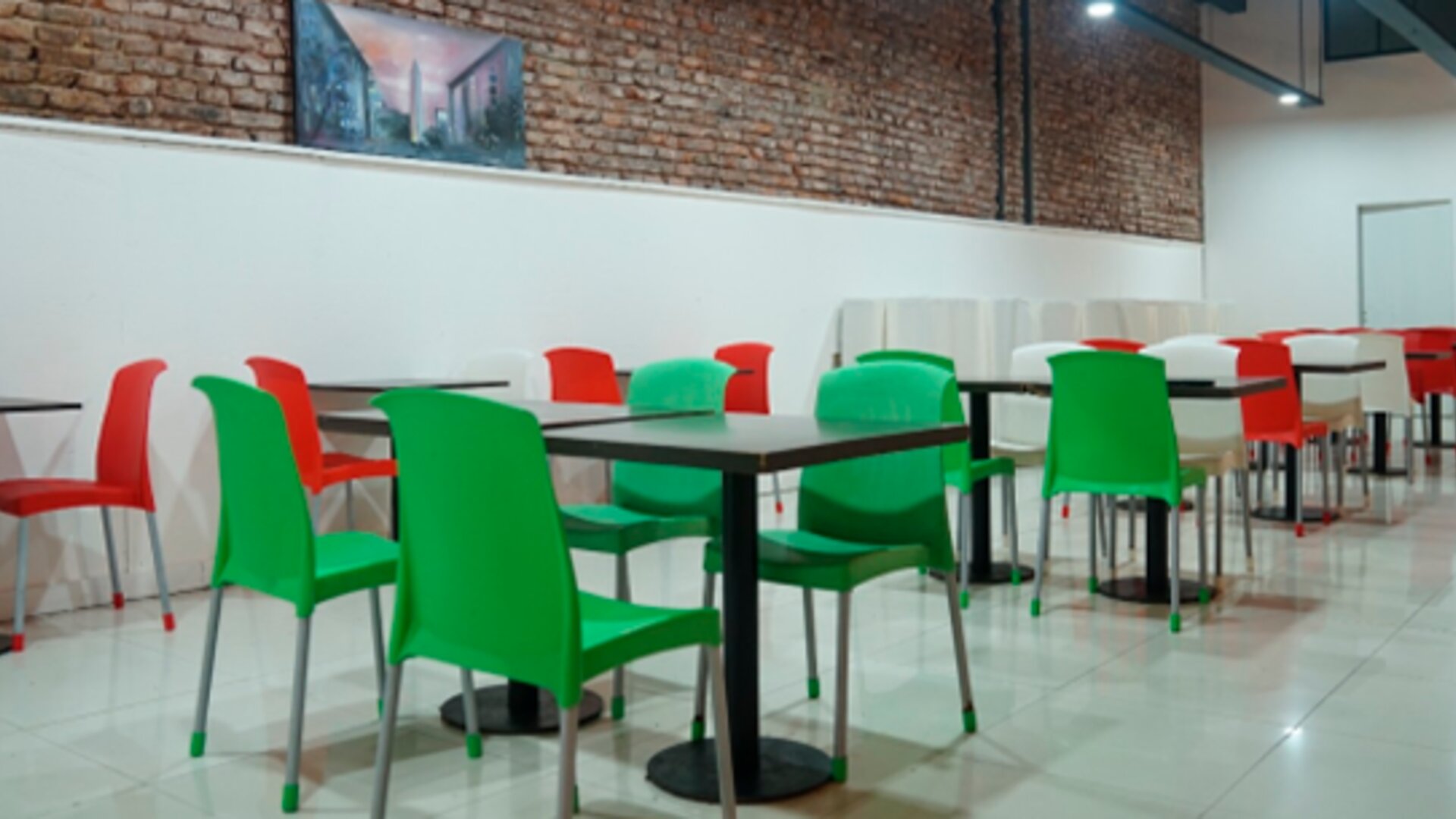 Dining area with red and green chairs, black tables, exposed brick walls and glossy tiled flooring at Bagu Buenos Aires.