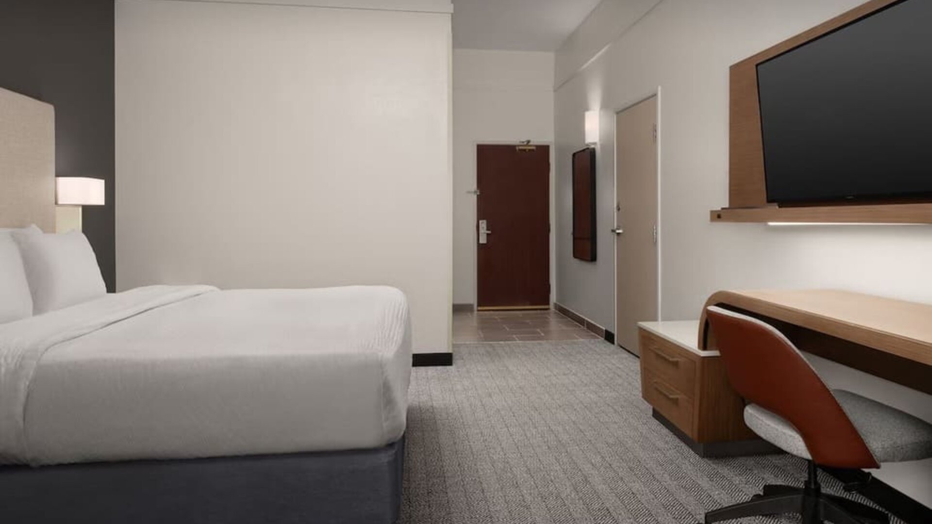 Guest room with white bed, wall-mounted television, wooden desk, office chair and gray carpeting at Courtyard By Marriott Dothan.