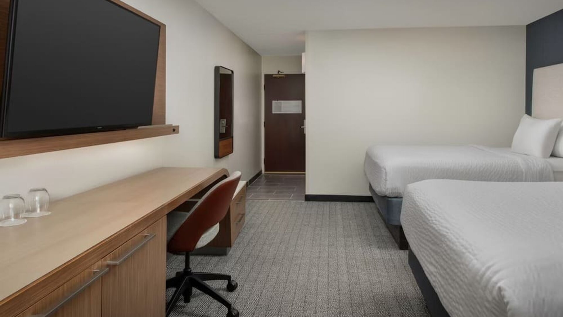 Guest room with two white beds, wooden desk, rust-colored office chair, television and gray patterned carpet at Courtyard By Marriott Dothan.