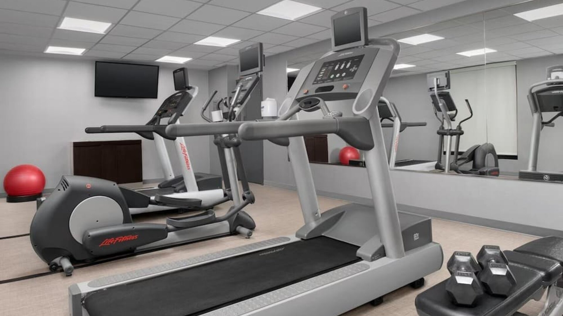Fitness center with treadmills, elliptical machines, dumbbells, wall mirrors and a red exercise ball at Courtyard By Marriott Dothan.