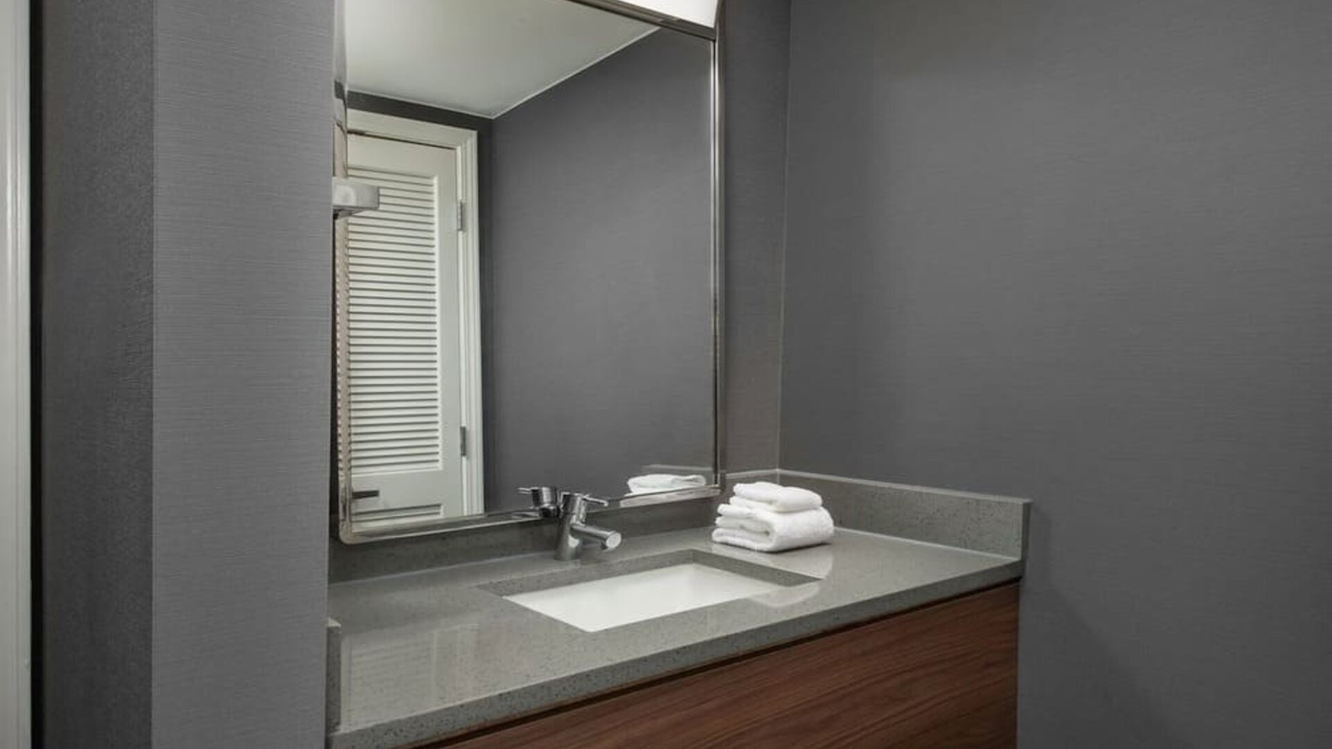 Bathroom vanity with gray countertop, inset sink, large mirror, wooden cabinetry and neatly folded white towels at Courtyard By Marriott Dothan.